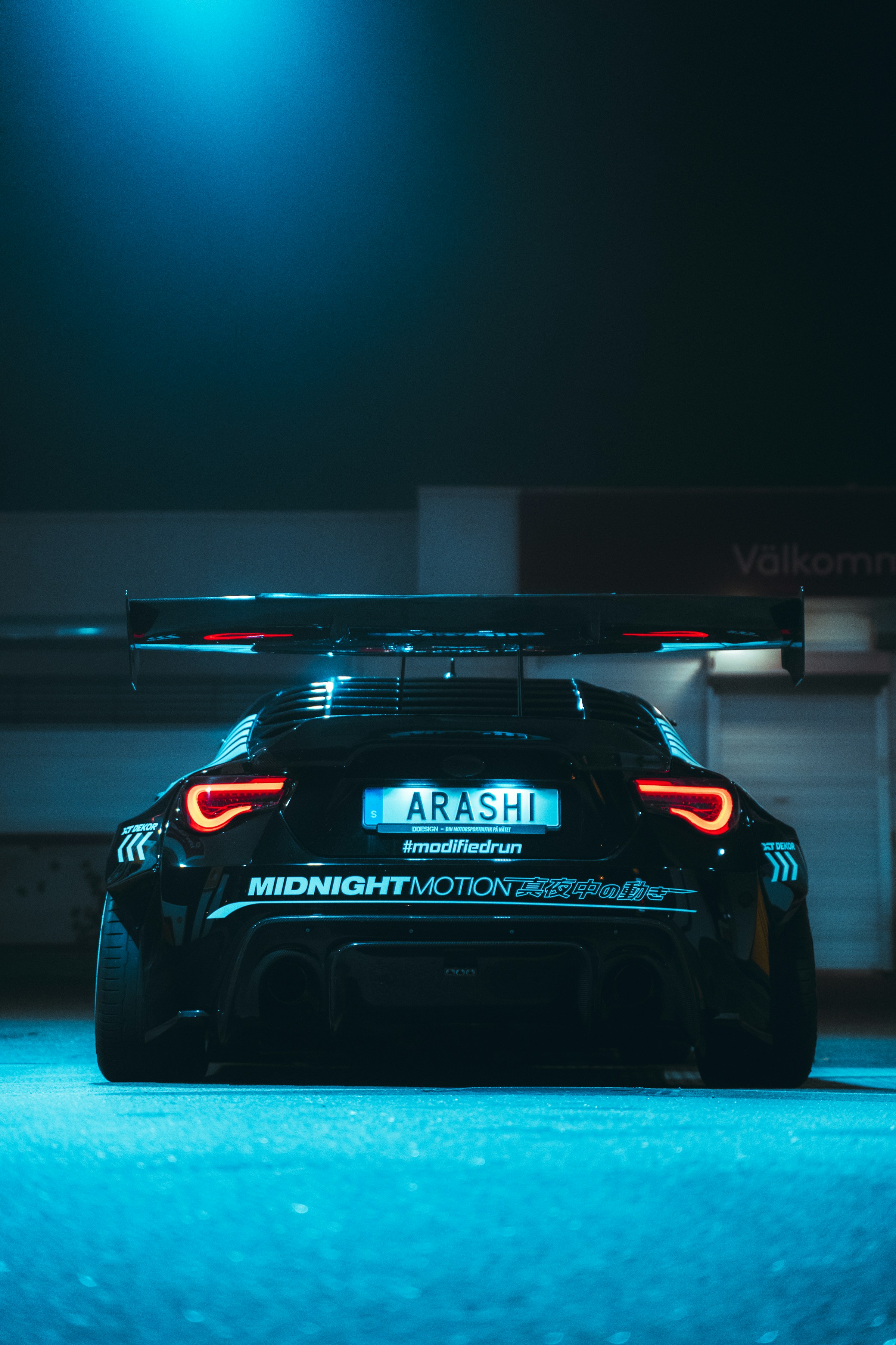 Modified black sports car glowing beneath garage lights